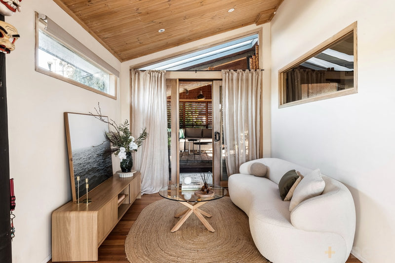Coastal home staging showcasing a neutral living area with curved sofa, timber ceiling, indoor-outdoor flow and soft styling designed to enhance buyer appeal.