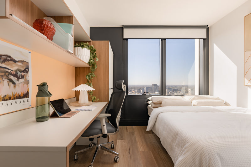 Modern bedroom with desk, chair, and city view window