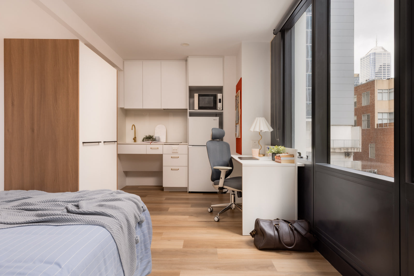 Modern bedroom with bed, wardrobe, desk, and kitchenette.