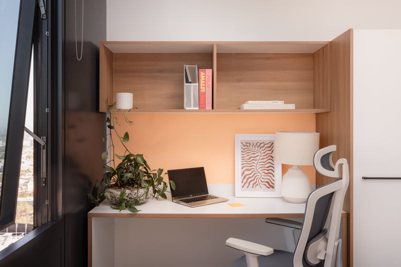 Modern home office with wooden desk, laptop, and chair near a window.